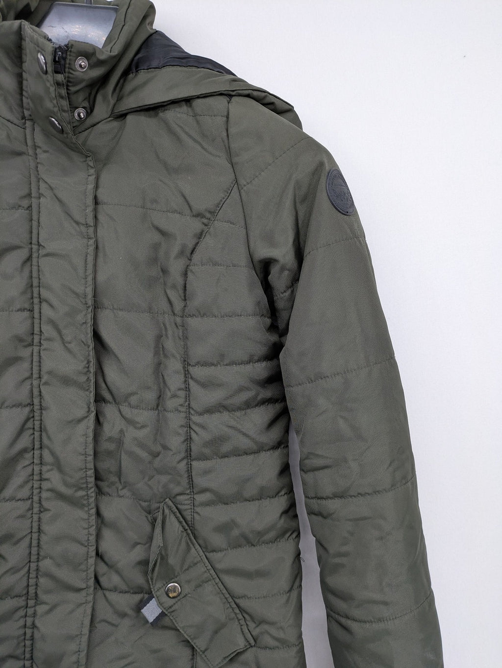 Vero Moda green puffer coat with quilted design and hood, featuring zipper and button closure.