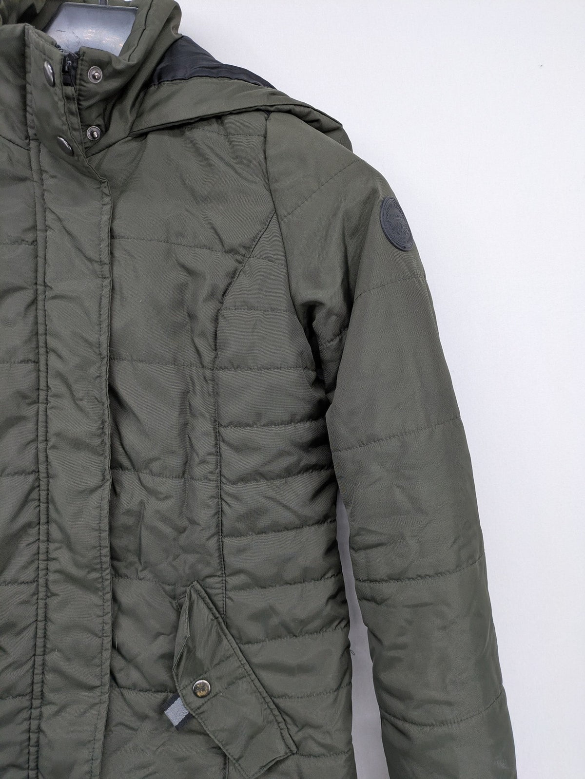 Vero Moda green puffer coat with quilted design and hood, featuring zipper and button closure.