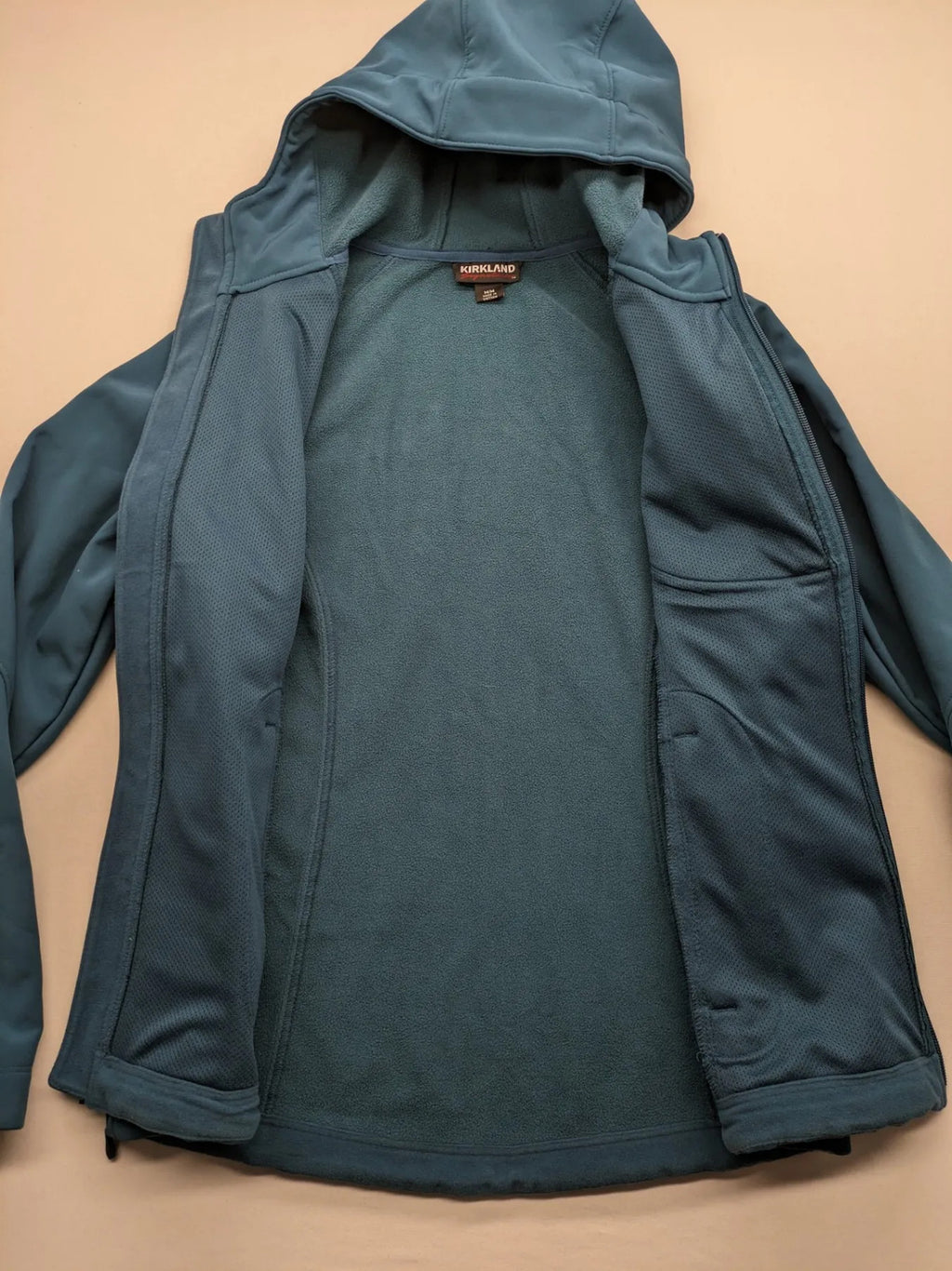 Kirkland Signature blue softshell jacket with hood, fleece lining, and zippered pockets.