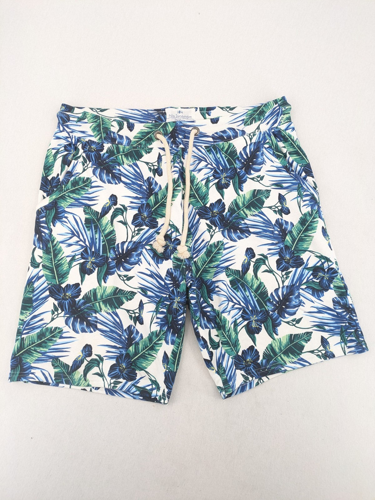 Nils Sundström blue and green tropical floral shorts with white background and elastic waistband.